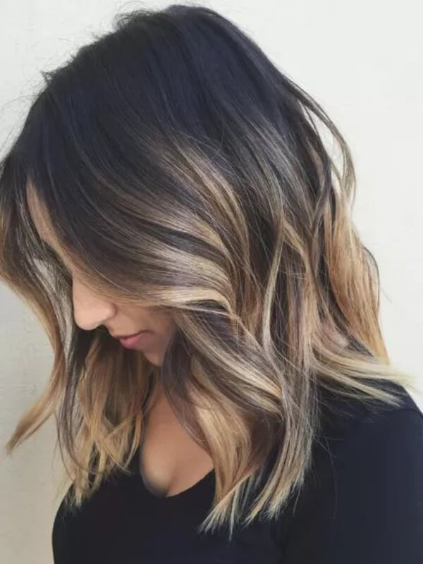 Sandy bronde highlights transition from deep espresso roots, giving the hair a luminous finish