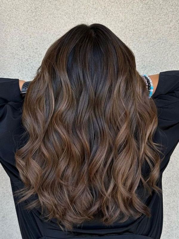 This chestnut balayage brings warmth and dimension to a chocolate brown base